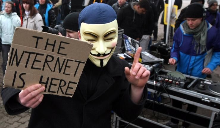 Protestor wearing a face mask associated with the hacker group 'Anonymous' titled 'The Internet is here'