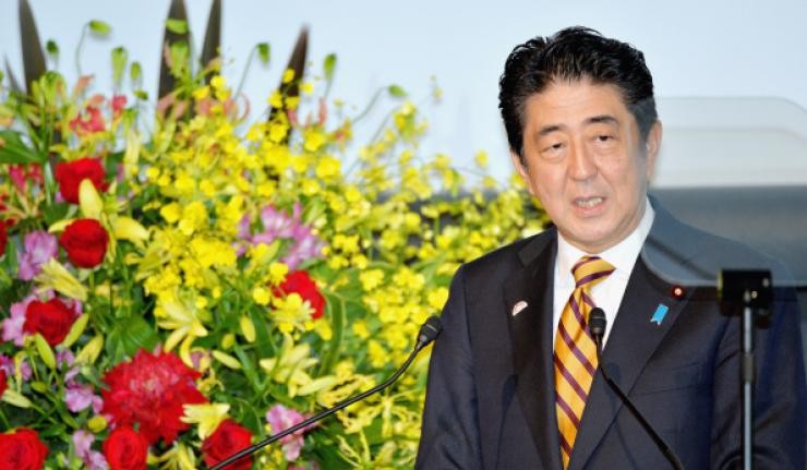 Shinzo Abe speaking to mics and cameras with a floral background