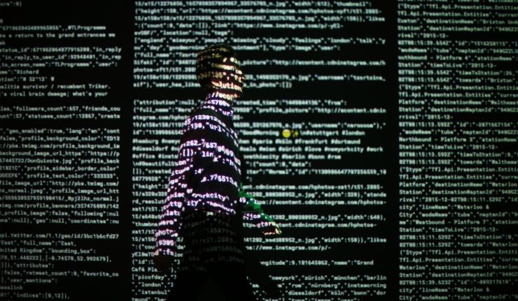 Man walking across a screen upon which code is being projected