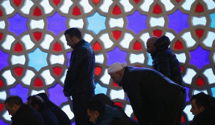 Muslims kneeling in prayer against a stained glass background