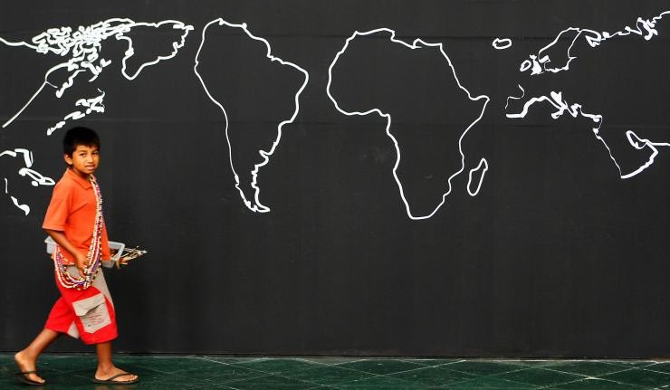 Child walking across a world map drawn on a blackboard