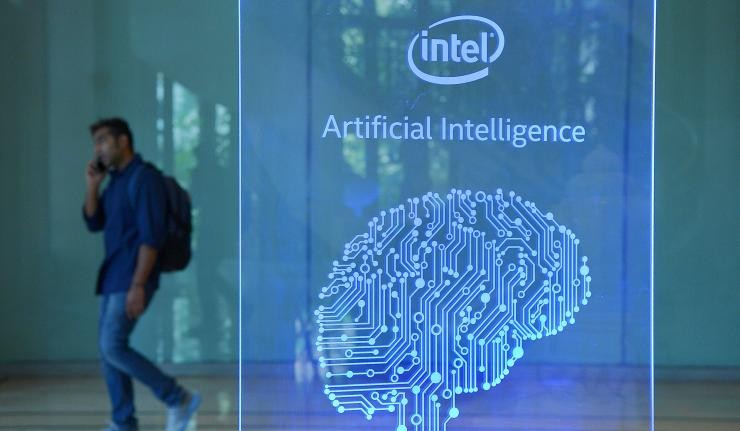 An engineer walking past a plaque which reads 'Intel Artificial Intelligence' An engineer walking past a plaque which reads 'Intel Artificial Intelligence'