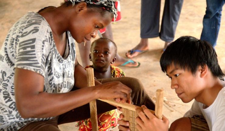 A Ghaneen mother and child and a volunteer building a wooden structure
