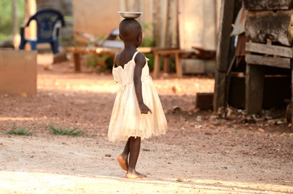 Little girl carrying water in a dish on her head