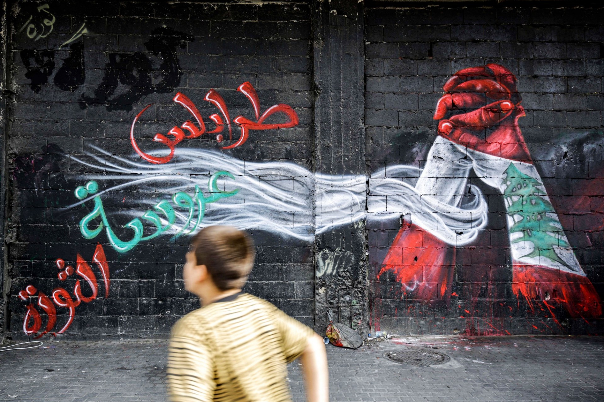 Child runs past a wall with abstract painting of Syrian flag