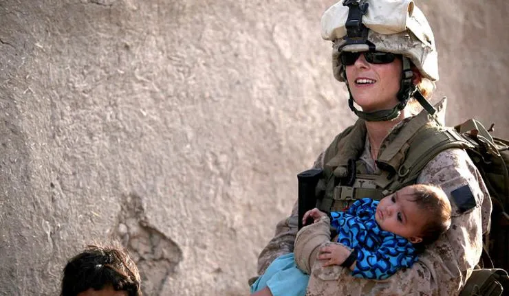 A US woman military officer carrying a child away from a conflict site in her arms