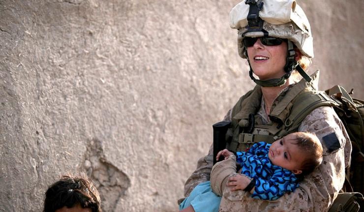 A US woman military officer carrying a child away from a conflict site in her arms