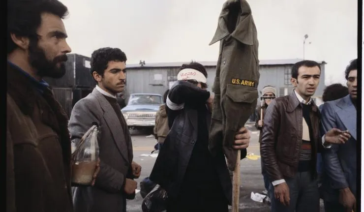 Iranian rebels holding up a US Army uniform on a stick likely ready to torch it