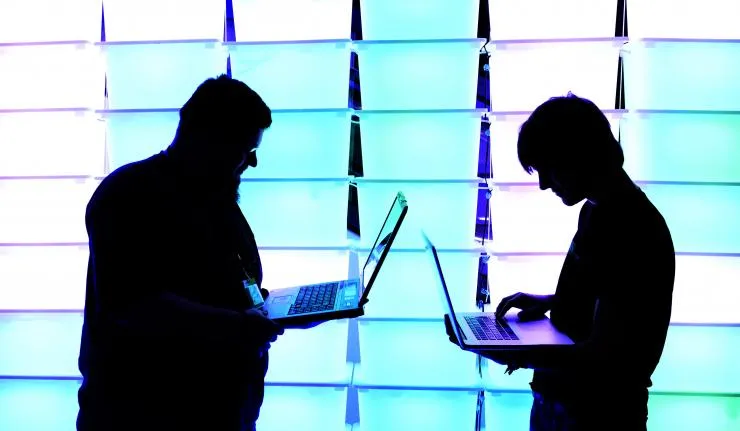 Sihouetted image of two coders holding laptops