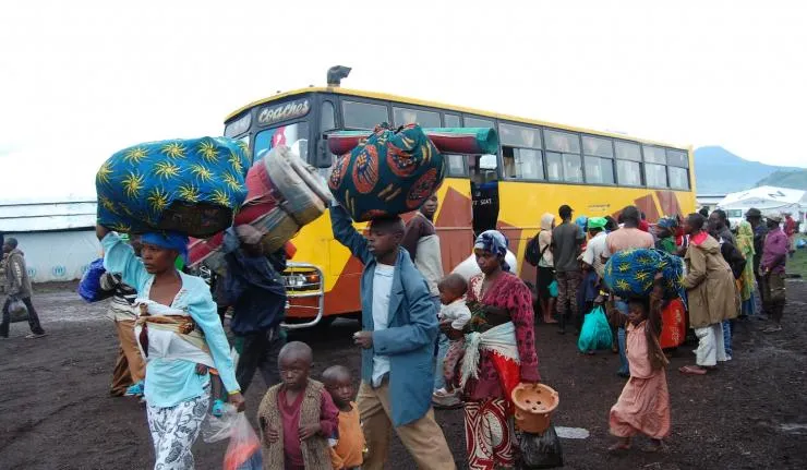 Congolese refugees by a bus carrying bags of clothes and pails