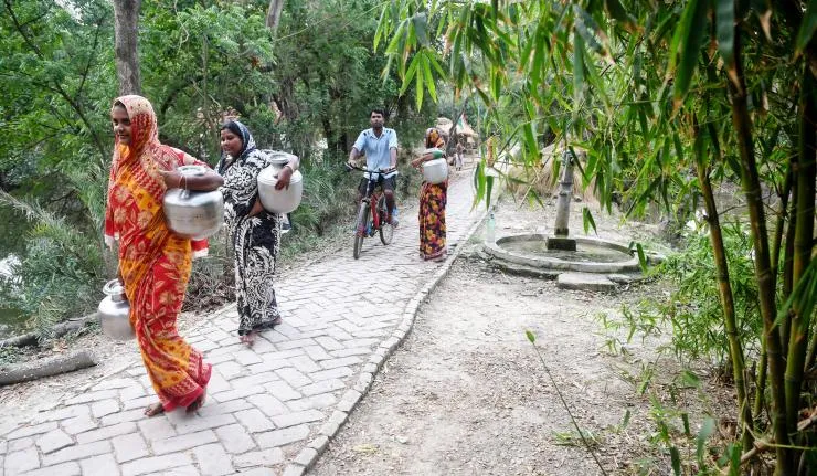 Women carrying pots walking on a paved path