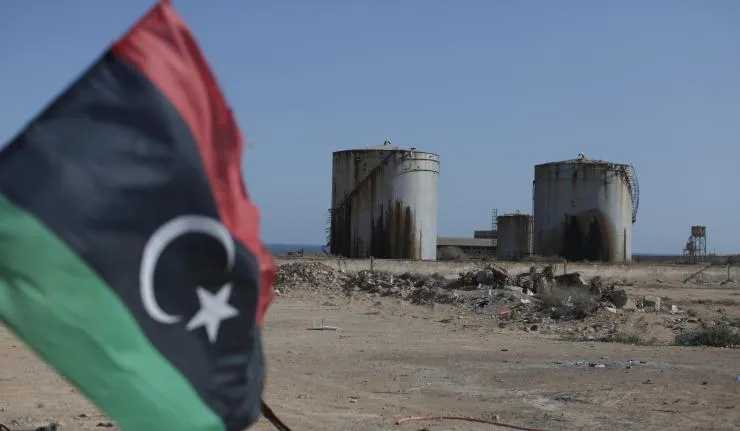 Dilapidated oil storage tanks with Libya flag in foreground