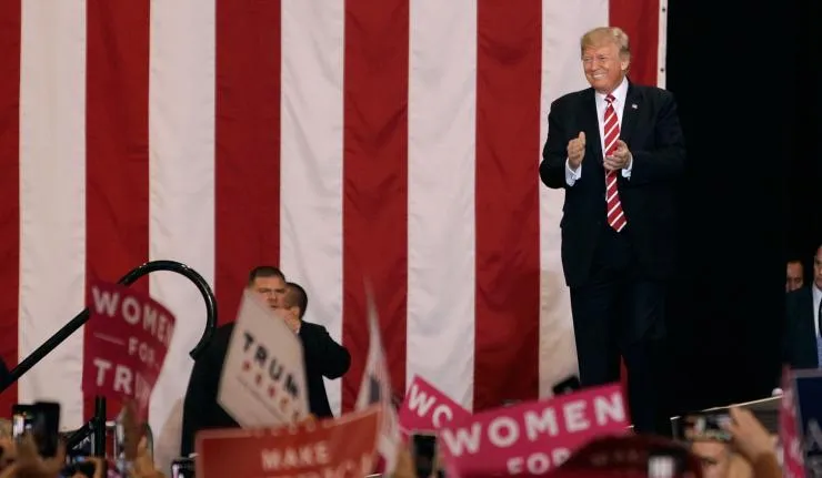 Donald Trump on stage smiling and applauding at a rally