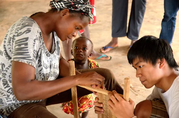 A Ghaneen mother and child and a volunteer building a wooden structure
